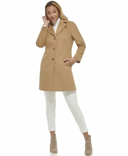 Woman in a brown coat and white pants posing.